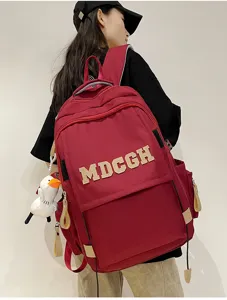 Détail d'un grand sac à dos rouge avec lettrage MDCGH et une breloque canard blanc