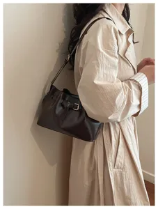 Zijaanzicht van een donkerbruine retro lederen onderarmtas met gespdetail op een beige jas