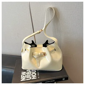 Detail van een glanzende crème bucket bag met gouden riemgesp op boekdecor