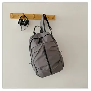 Mochila de nailon gris minimalista colgada en un perchero de madera en pared blanca.
