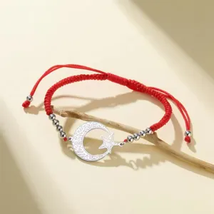 Detalle del dije de luna y estrella de acero inoxidable en pulsera roja ajustable
