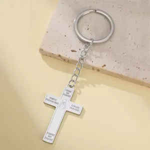Close-up of stainless steel cross keychain with French religious engraving on stone.