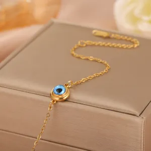 Close-up detail of a gold stainless steel Evil Eye charm bracelet on a jewelry box