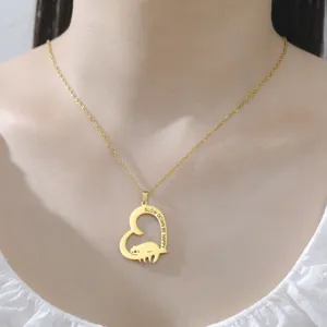 Detailopname van gouden hartjesketting met luiaard en de tekst "Slow Down" gegraveerd.