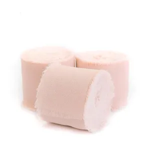 Nahaufnahme von drei Rollen rosa Chiffonband mit Fransen für DIY Hochzeitskarten