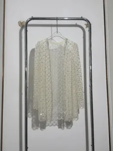 Detailed view of a white lace cardigan featuring intricate sequin and bead embellishments.