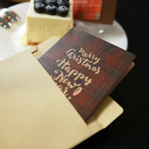 Festive plaid Christmas holiday greeting card with kraft paper envelope on a cafe table