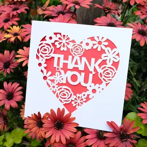 Elegant laser-cut heart-shaped Thank You greeting card nestled in a bed of vibrant daisies