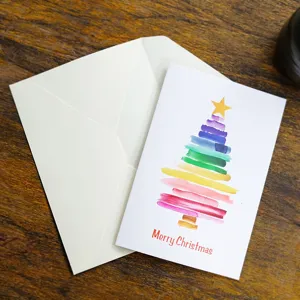 Handcrafted watercolor Christmas tree greeting card with ivory envelope on wood