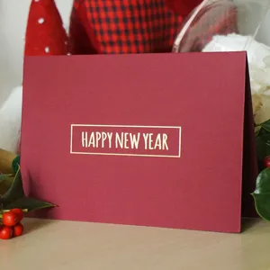 Elegante tarjeta de felicitación roja con texto HAPPY NEW YEAR dorado y motivos festivos