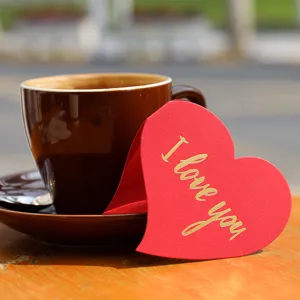 Red heart-shaped greeting card with gold I love you text on a wooden table.