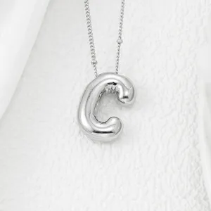Détail de pendentif lettre C argenté gonflé montrant une texture métallique lisse.