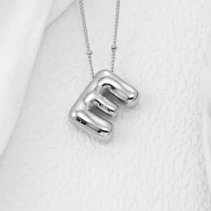 Gros plan détaillé d'un pendentif lettre argenté gonflé tendance, finition lisse, chic.