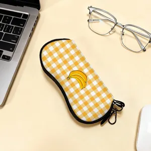 Vista dettagliata di un astuccio per occhiali a scacchi gialli con stampa banana su scrivania.