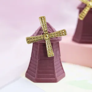 Close-up of purple velvet windmill ring box, gold propeller detail, soft pastel background.
