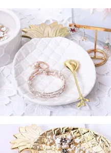Close-up view of white ceramic pineapple jewelry dish with gold leaf trim, elegant home decor.