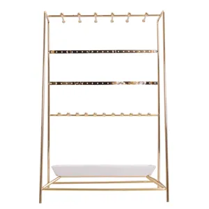 Support de bijoux en métal doré avec plateau blanc pour boucles d'oreilles et bagues.