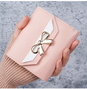 Close-up of pink women's short wallet featuring a stylish gold bow and white trim