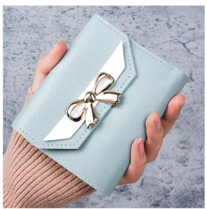 Close-up of light blue women's short wallet featuring a elegant gold bow decoration.