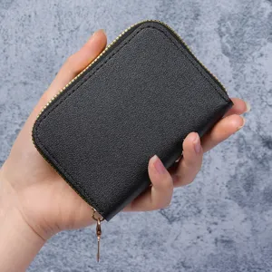 Petit porte-cartes accordéon noir avec fermeture éclair dorée tenu en main pour l'échelle.