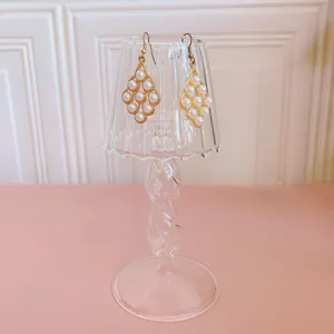 Clear glass lamp earring display stand with chic pearl earrings for jewelry photography.