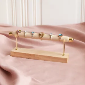 Wooden ring display stand detail, beige velvet roll and gold metal rods on pink cloth background.