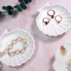 Detailed view of white shell jewelry dish displaying delicate pearl necklace and crystal rings.