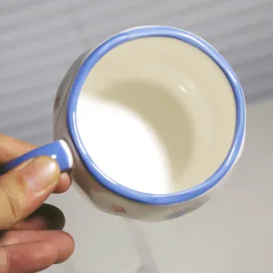 Taza de café de cerámica artesanal con borde azul y asa bonita para latte art y bebidas.