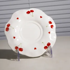 Platito de café de cerámica pintado a mano con motivo de cereza roja y borde festoneado.