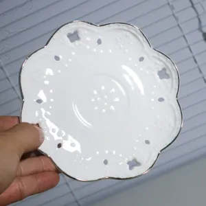 Witte keramische koffieschotel met zilveren rand en mooi bloemvormig opengewerkt design.