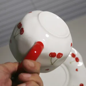 Vista detallada de la taza de café de cerámica artesanal con forma única y patrón de cereza.