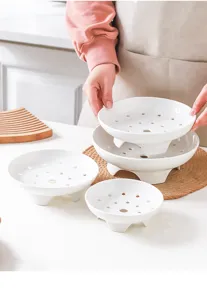 Close up view of white ceramic steamer plates with high feet and functional steam drainage holes.