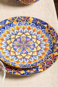 Nahaufnahme eines bohemischen Keramiktellers mit buntem Mandala Muster auf Tischdecke.