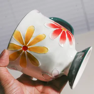 Detailansicht der Keramiktasse mit geprägtem bunten Blumenmuster und grünem Sockel.