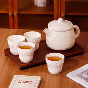 Service à thé en céramique avec théière et quatre tasses sur plateau en bois, élégant.