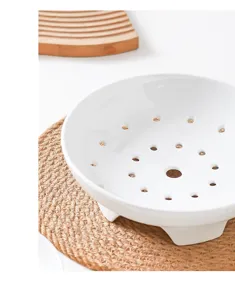 Close-up detail of white ceramic steamer dish with ventilation holes and raised feet for cooking.