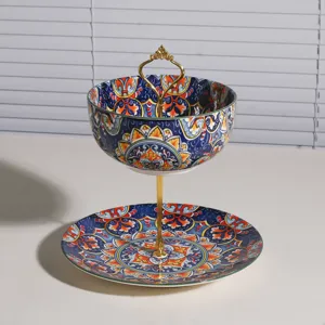 Frutero de cerámica de dos niveles con diseño bohemio azul naranja y asa dorada elegante.
