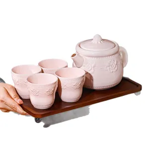 Service à thé en céramique rose avec théière et quatre tasses sur plateau en bois maison.