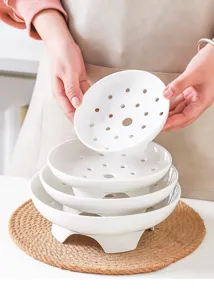Detailed view of white ceramic steamer plate, stacked layers with breathable drainage holes.