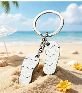Macro view of silver metal flip-flop keychain charms on a sunny beach sand backdrop.