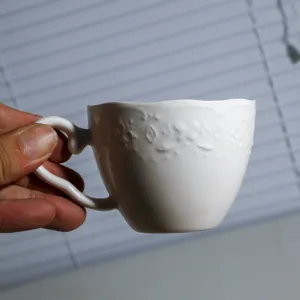 Witte keramische koffiekop met in reliëf gemaakte patroon, elegante kleine porseleinen kop.