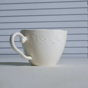 Vista detallada de taza de café de cerámica blanca con elegante patrón en relieve y asa.