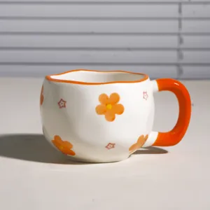 Vista detallada de taza de café de cerámica hecha a mano con patrón de flores naranjas.