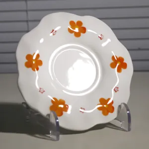 Platito de café de cerámica con borde ondulado y patrón de flores naranjas, detalle.