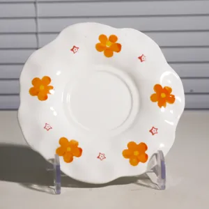 Platito de café de cerámica pintado a mano con bonito motivo de flor naranja y borde ondulado.
