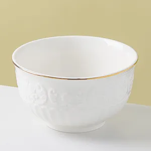 Close-up detail of white ceramic bowl with elegant gold rim and exquisite embossed floral pattern.