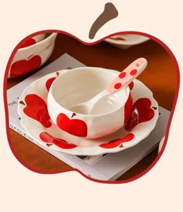 Dettaglio set ciotola e piatto in ceramica, con motivo a mela rossa sottosmalto e cucchiaio.