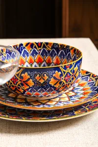 Dettaglio set stoviglie in ceramica boho, ciotola e piatti con vivace motivo floreale blu.