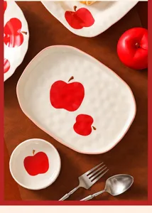 Dettaglio del set di stoviglie in ceramica con grazioso motivo a mela rossa sui piatti.