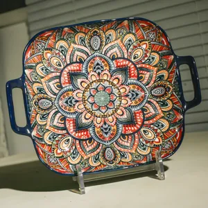 Close-up of square ceramic baking dish with double handles, vibrant bohemian mandala pattern.